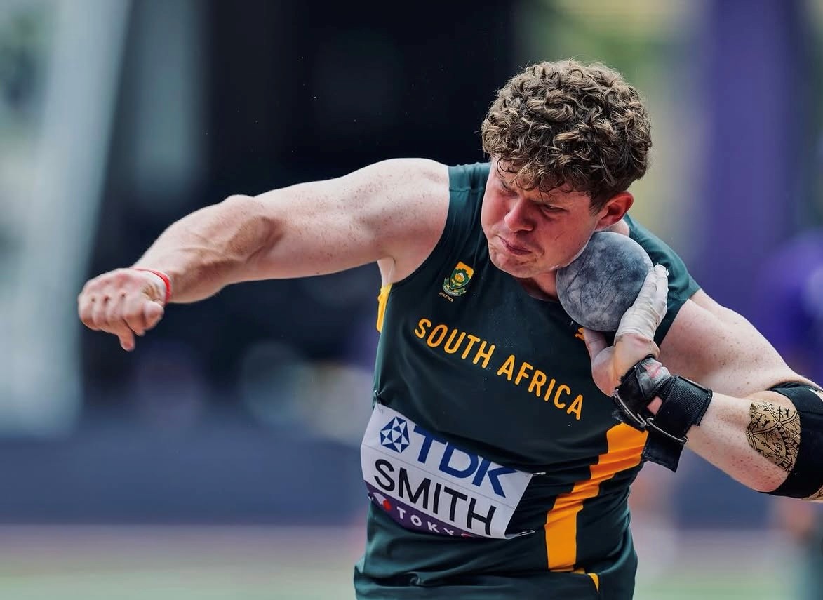 South African track and field athlete in green and gold launching a shot put during a throw contest, focused on the ball in his hand.