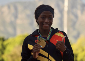 Young girl athlete proudly displays a gold medal with a striped ribbon and gives a thumbs-up.