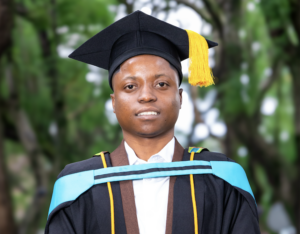Graduate in cap and gown posing outdoors, wearing a blue stole and yellow tassel for commencement.