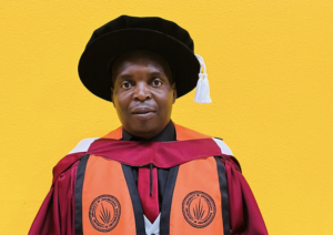 Person in doctoral gown and black cap with tassel, against a bright yellow background.