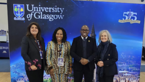 Four professionals posing in front of a University of Glasgow banner, smiling at the camera.