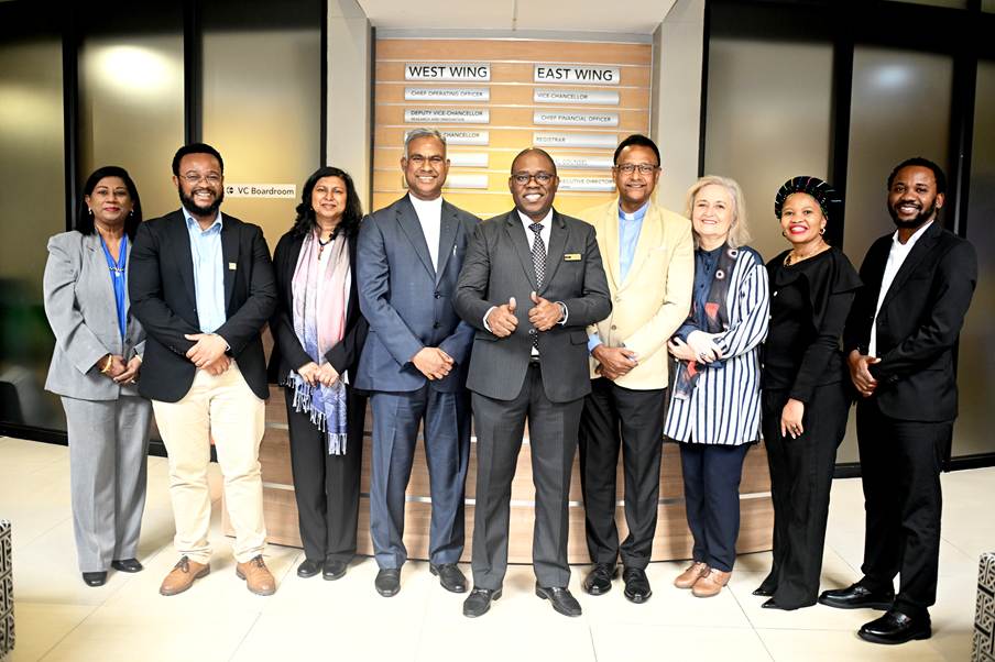 Group of ten professionals in business attire posing in a modern office lobby, with a West Wing / East Wing directory behind them.