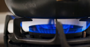 Close-up of a gas stove burner with a bright blue flame beneath a pot ring.