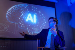 Man in a suit presenting beside a projection of a glowing blue brain and AI graphics in a dark room.