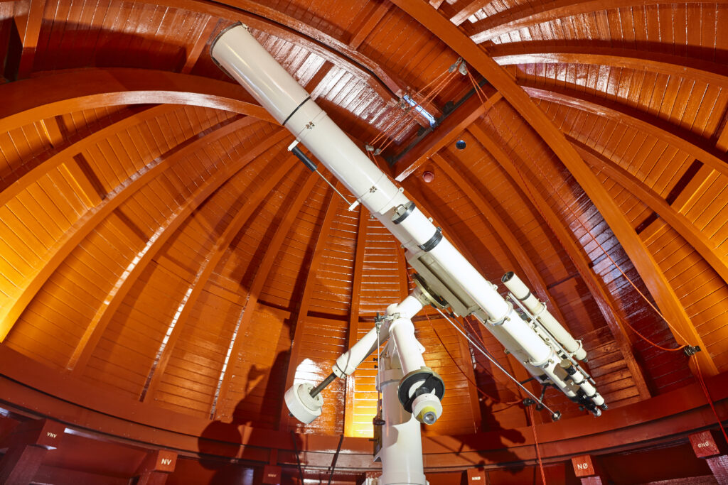 Interior of an observatory dome with orange wooden ribs and a large white telescope mounted on a central support,