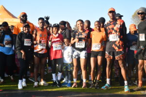 Group of runners at the race start on a sunny day, bib numbers visible on their shirts