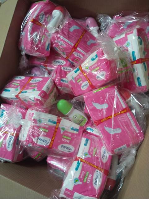 Cardboard box full of many pink packaged items wrapped in plastic, with a few green items visible among them.