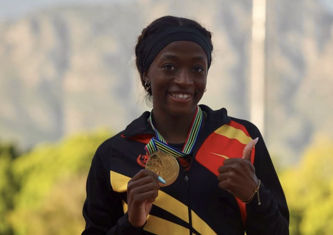 Young girl athlete proudly displays a gold medal with a striped ribbon and gives a thumbs-up.