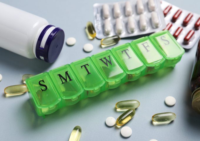 Different pills, organizer and medical jars on light background, closeup