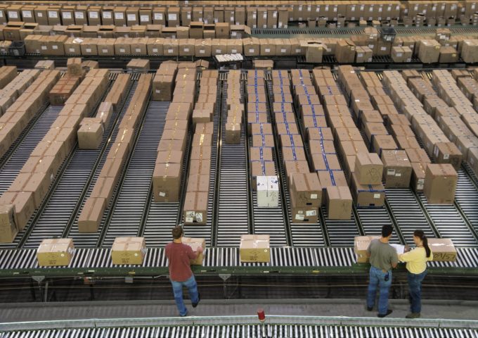 Overview of a large industrial distribution warehouse storing products in cardboard boxes on conveyor belts and racks.