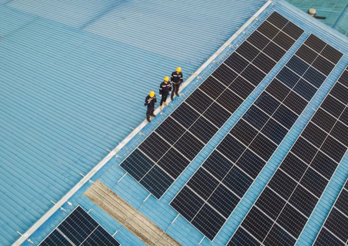Aerial view of engineer worker walking on rooftop checking on solar cell panels installed on roof of the factory with professional team. Electric power industry renewable energy.
